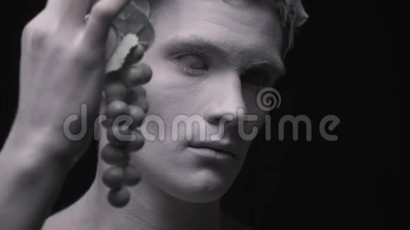 戴着月桂花圈的人的雕像拿着一串葡萄眨着眼睛视频的预览图