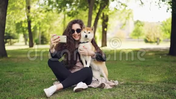 快乐的博客宠物主人正在和她的狗用智能手机自拍人类和动物坐在草坪上视频的预览图