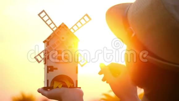 一个女孩站在向日葵的田野里在夕阳的映衬下手里拿着一个玩具风车磨坊开进来了视频的预览图