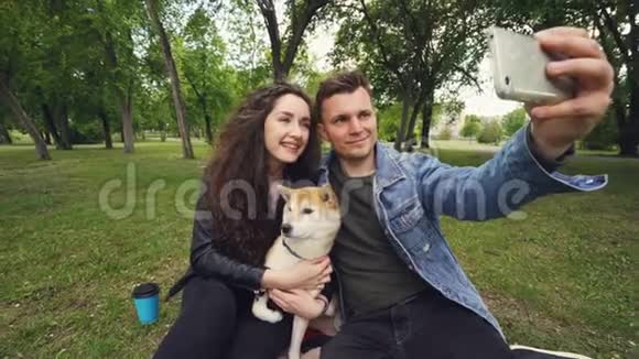 一个快乐的男人拿着智能手机自拍吻着他的妻子而她却抱着可爱的狗吻着它视频的预览图