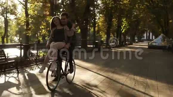 微笑的年轻夫妇骑着同一辆黑色自行车背景是太阳光女孩坐在舵上视频的预览图