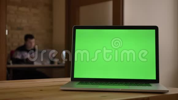 笔记本电脑绿色屏幕特写镜头躺在办公室的办公桌上室内有商人在处理模糊的电脑视频的预览图