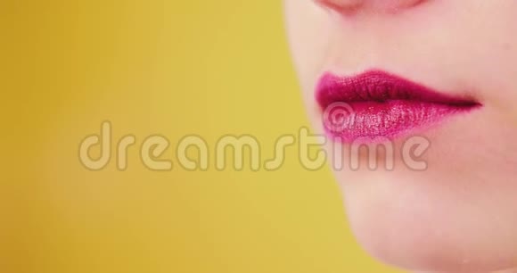 特写的亮粉色的女性嘴唇在一个黄色的背景上被工作室隔离微笑肖像满足喜悦视频的预览图