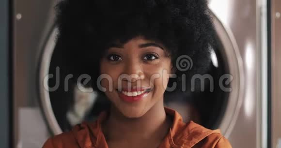 年轻微笑的非洲裔美国妇女站在自助洗衣店的肖像视频的预览图