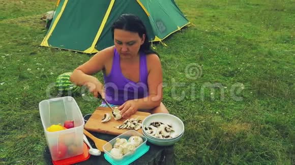 帐篷附近的一个林间空地上一个女人在树桩上剪了一个蘑菇蘑菇上面放着香槟作为一张桌子视频的预览图