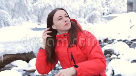 女人坐在冬天森林里的一条山河的河岸上梳头视频的预览图