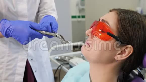 当医生站在病人旁边时年轻的女人害怕拔掉一颗牙齿坐在牙科椅上抱着病人视频的预览图