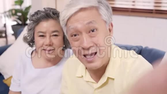 亚洲老年夫妇在家客厅里躺在沙发上与孙子一起使用智能手机视频会议视频的预览图