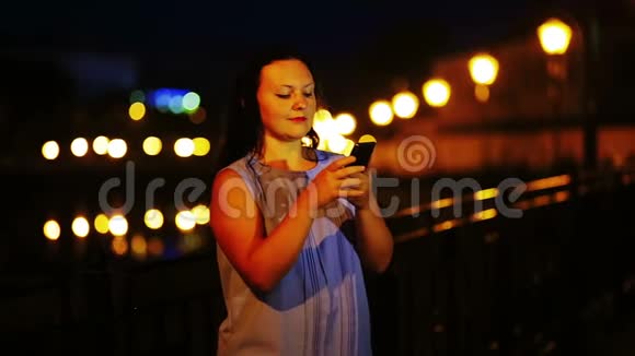 一个年轻的女孩在夜空的背景下用手机在信使上写字视频的预览图