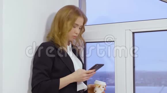 年轻女子用手机浏览电子邮件手拿咖啡杯视频的预览图