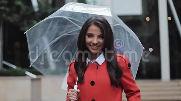 美丽的年轻商务女性穿着红色外套在雨天走在街上微笑着拿着雨伞她是视频的预览图