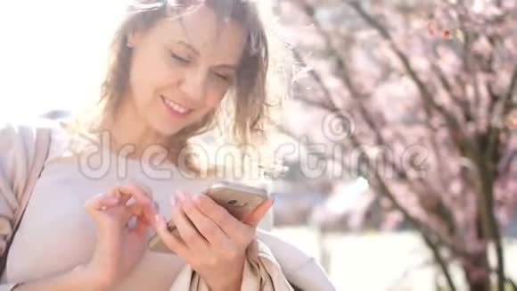 一位手里拿着智能手机的年轻女子的亲密肖像女孩微笑着在手机里翻阅照片视频的预览图