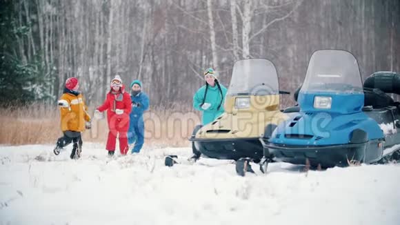 冬季森林幸福的家庭穿着五颜六色的衣服在雪地摩托附近玩雪球奔向镜头慢慢视频的预览图