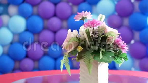 花瓶里的花放在旋转的桌子上背景是蓝色和紫色的气球视频的预览图