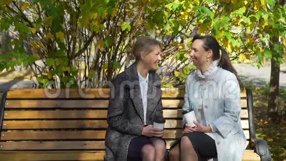两个女人坐在长凳上在秋天的公园里聊天视频的预览图