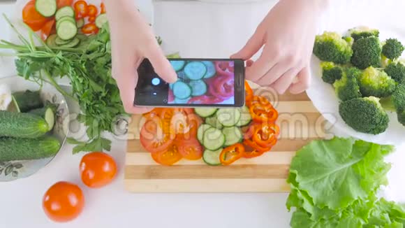 女人手拿着智能手机正在为沙拉拍摄新鲜蔬菜的照片切片在切割板上视频的预览图