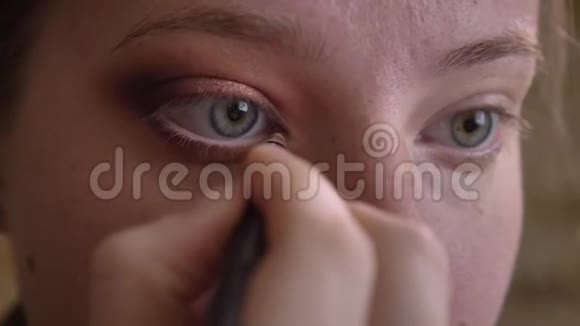 年轻的白种人女性化妆师在她的下眼睑上涂白色眼线的特写肖像视频的预览图