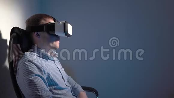 一个穿衬衫的年轻人坐在椅子上使用虚拟现实耳机视频的预览图