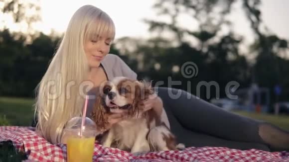 美丽的白种人金发女人在公园里带着她的狗在草地上放松抚摸着她拥抱着她视频的预览图