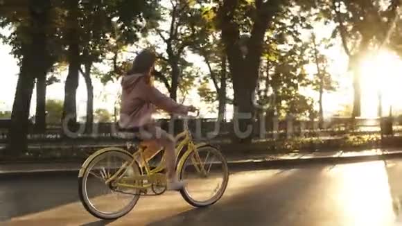 夏天的城市公园里漂亮的小女孩骑着黄色的自行车在街上背景上的树木和阳光视频的预览图