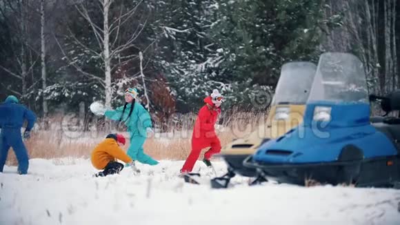 冬季森林年轻的幸福家庭穿着五颜六色的衣服在雪地摩托附近玩雪球慢动作视频的预览图