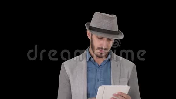 戴着帽子走路使用平板电脑阿尔法频道的英俊微笑阿拉伯男子视频的预览图