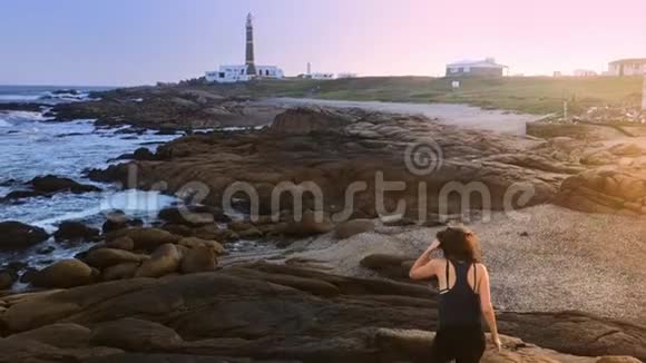 那个女孩在日落时沿着灯塔附近的海岸散步视频的预览图