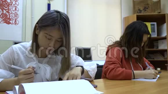 两个亚洲学生的女孩在教室里用笔记本学习视频的预览图