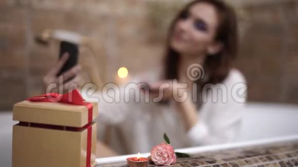 年轻女子带着鲜艳的妆容自拍坐在浴缸里用红酒杯可爱的女孩在浴室里放松视频的预览图