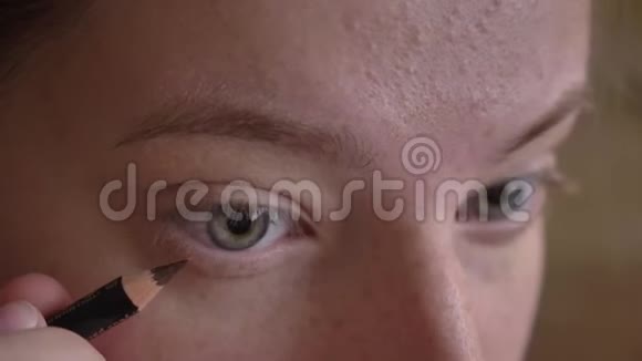 年轻白种人女化妆师用棕色眼线涂在她的下眼睑上的特写肖像视频的预览图