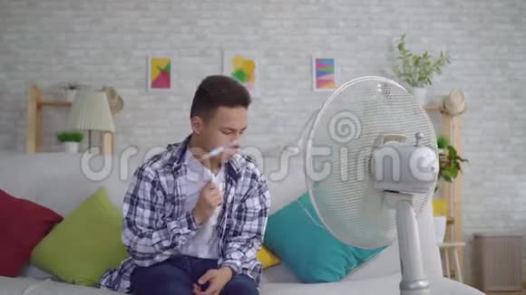 年轻的亚洲男人从坐在工作风扇前的热气中拯救了热的概念视频的预览图