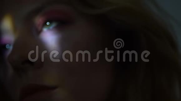 美丽的女性脸被五颜六色的灯光照亮黑暗特写视频的预览图