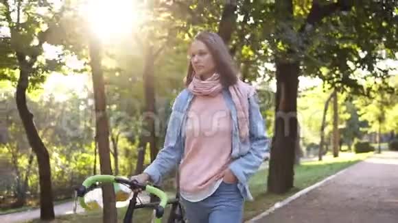 早晨公园里一位年轻女子在自行车旁散步的正面景色那个女孩骑着她的徒步自行车走路视频的预览图