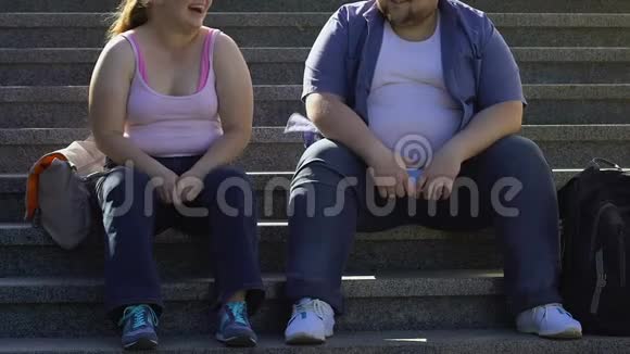 胖乎乎的学生在说着笑坐在大学附近的楼梯上朋友们视频的预览图