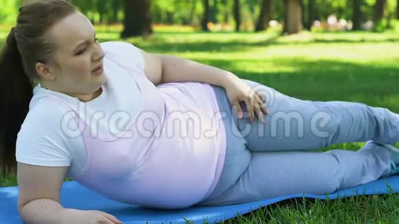 肥胖的女孩在户外运动试图抬起她的腿减肥运动视频的预览图
