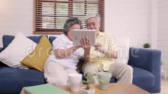 亚洲老年夫妇在家客厅里用平板电脑看电视视频的预览图
