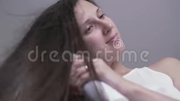 那个女孩用吹风机吹干头发一个没有化妆的年轻女孩用吹风机擦干头发早上的造型视频的预览图