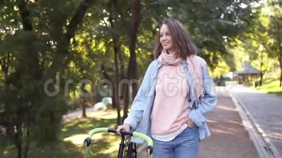 快乐的微笑的女孩在早晨公园里除了一辆自行车外还散步那个女人骑着她的自行车走路手里拿着视频的预览图