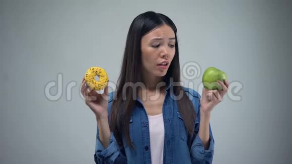 饥饿的女孩试图在甜甜圈和苹果之间做出选择健康的饮食诱惑视频的预览图