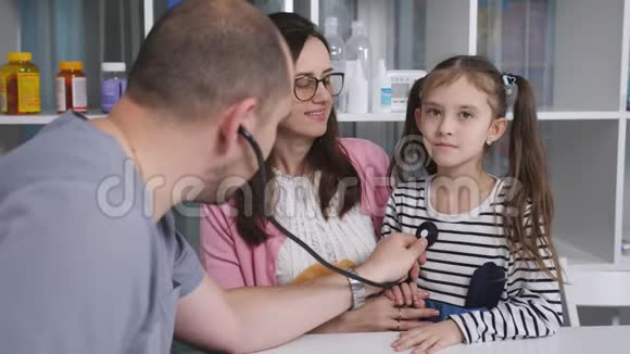 家庭男医生用听诊器倾听胸部小女孩母亲拥抱和安慰女儿视频的预览图