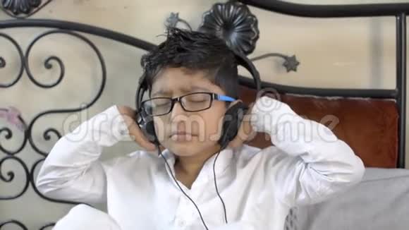 戴眼镜戴眼镜戴耳机闭上眼睛双手放耳机听音乐的印度小白种人男孩视频的预览图