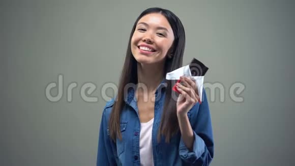 迷人的亚洲女孩在镜头前微笑吃黑巧克力广告视频的预览图
