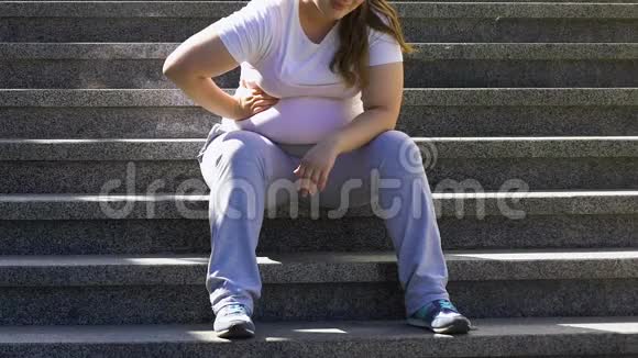 患背痛的肥胖女孩锻炼后坐在楼梯上视频的预览图