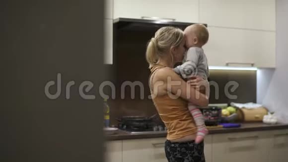 妈妈把一岁的女儿抱在怀里抱着她的拥抱厨房人工照明孩子很高兴视频的预览图