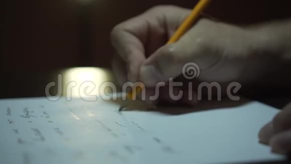 男人在房间的纸上手写男性在昏暗光线下在纸上写字的特写镜头视频的预览图