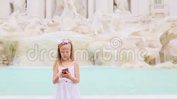 可爱的小女孩与智能手机温暖的一天户外欧洲城市附近著名的丰塔纳迪特雷维视频的预览图