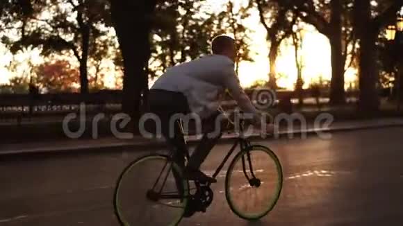 快乐的年轻人骑一天快乐的年轻人骑着自行车在空车路上穿过绿树公园视频的预览图