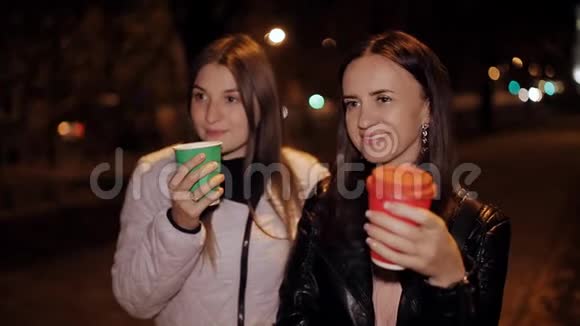两个微笑的朋友晚上在街上的肖像手里拿着咖啡视频的预览图