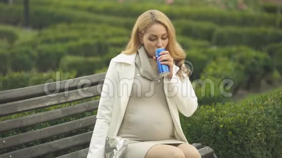 孕妇吃薯片喝软饮料坐在公园里吃不健康的食物视频的预览图