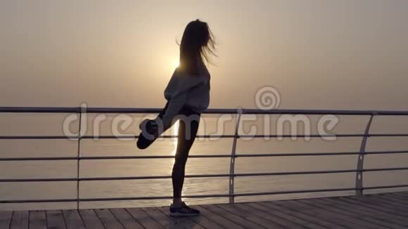 长发女孩伸展着腿眺望大海黎明日出运动服紧身裤帽衫外壳视频的预览图
